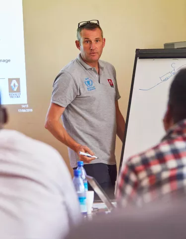 Man standing next to a white board talking to other people seated